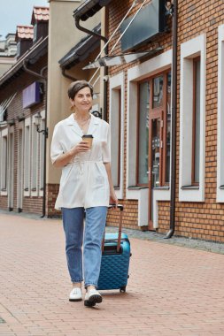Elinde kağıt bardakla gezen mutlu yaşlı bir kadın ve yanında bavulla yürüyen, paket kahve, şehir yaşam tarzı.