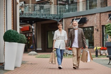Mutlu yaşlı çift alışveriş yapıyor, yaşlı adam ve kadın el ele tutuşuyor ve sokakta yürüyor.
