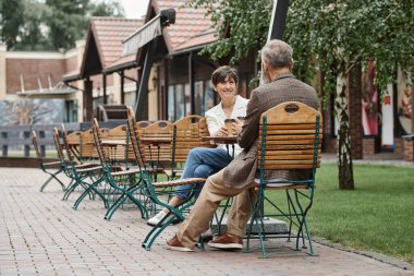 Mutlu yaşlı kadın ve adam, açık kafede kahve içiyor, teras, yaz, sandalyeye oturuyor.