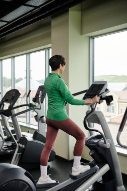 aktif son sınıf, spor giyinen yaşlı bir kadın spor salonunda egzersiz yapıyor. Adımlı egzersiz makinesi kullanıyor, spor yapıyor.