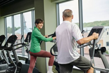 Aktif yaşlılar, spor salonunda yaşlı bir adama bakan mutlu bir kadın, birlikte egzersiz yapan yaşlı bir çift.