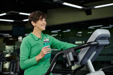 Mutlu yaşlı kadın elinde suyla spor şişesi tutuyor ve başka tarafa bakıyor, spor, spor, spor, spor, spor