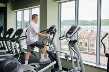 Sakallı adam stepper makinesinde çalışıyor, yaşlılar spor salonunda, aktif son sınıf, fitness ve spor