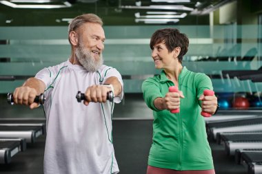 Mutlu yaşlı çift, mutlu erkek ve kadın halterli antrenman, karı koca spor salonunda.
