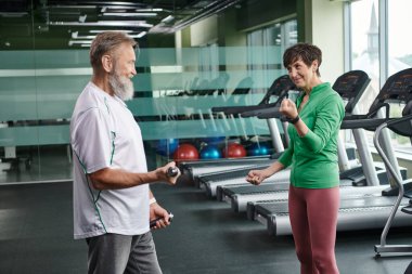 Mutlu kadın sakallı adama bakıyor spor salonunda dambıllarla çalışıyor, aktif yaşlılar, yaşam tarzı...