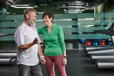Mutlu kadın sakallı adamı cesaretlendiriyor spor salonunda dambıllarla çalışıyor, aktif yaşlılar, yaşam tarzı...