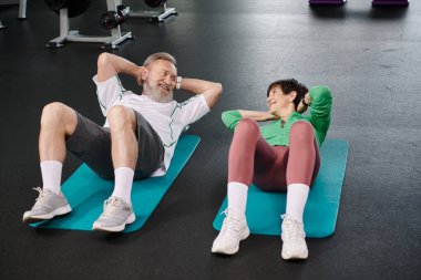 Yaşlı adam ve kadın mekik çekiyorlar, aktif yaşlılar spor salonundaki spor paspasları üzerinde egzersiz yapıyorlar, sağlıklı bir hayat sürüyorlar.