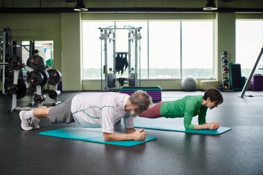 Yaşlı bir adam ve kadın spor salonundaki aktif son sınıf öğrencileri, sağlıklı yaşam üzerine tahta döşeme yapıyorlar.