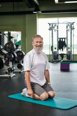 Sakallı mutlu yaşlı adam fitness minderinde oturuyor, aktif son sınıf öğrencisi, enerjik ve sağlıklı, pozitif