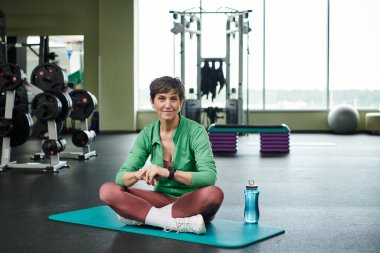 Keyifli yaşlı kadın bacak bacak üstüne atmış, spor şişesi suyla dolu, aktif.