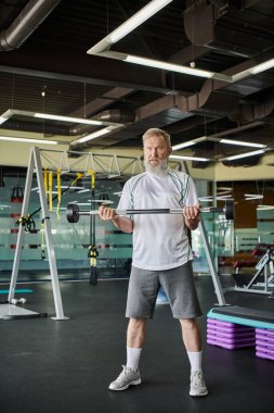 Sakallı yaşlı atletik bir adam spor salonunda halterle çalışıyor, son sınıf öğrencisi, sporcu, güçlü.