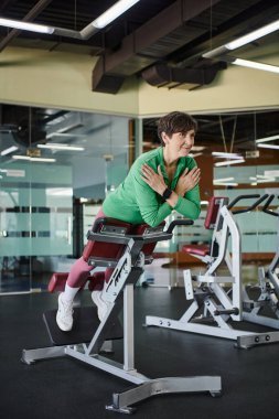 Kısa saçlı yaşlı kadın spor salonunda çalışıyor, aktif, motivasyon, egzersiz makinesi, gülümseme