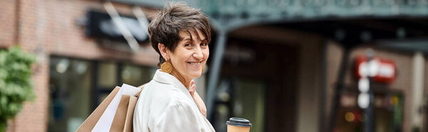 banner, cheerful senior woman with short hair holding shopping bags and coffee to go near outlet