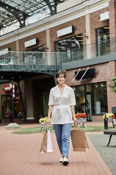 pleased senior woman walking with shopping bags on urban street, retail, elderly in city, outdoors