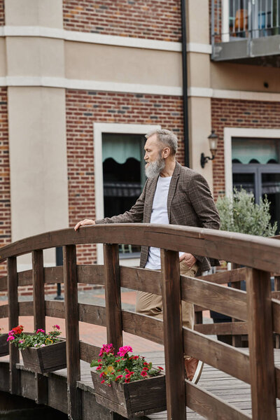 aging population, bearded man standing on wooden bridge, thinking and looking away, city life