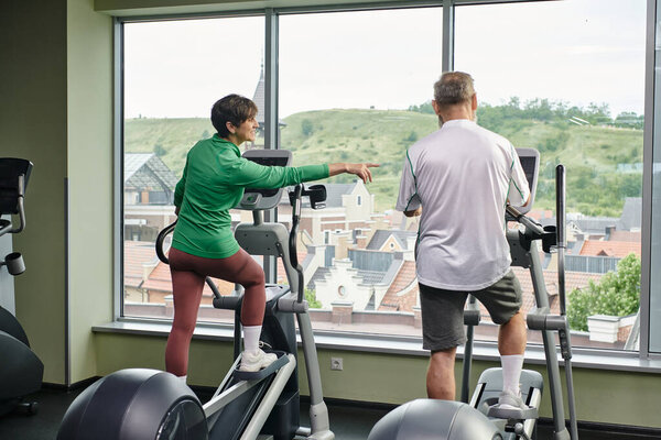 active seniors, woman pointing at stepper exercise machine near elderly man, senior couple, sport