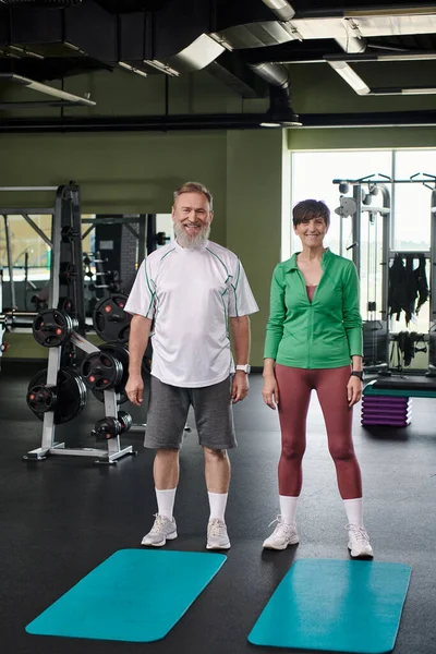 stock image happy elderly couple standing near fitness mats, looking at camera, full length, active seniors