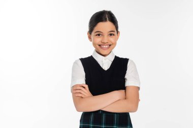 happy schoolgirl in black vest standing with folded arms and looking at camera isolated on white clipart