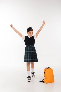 Neşeli kız sırt çantasına bakıyor ve elleri açık duruyor, yaşasın, okul konseptine geri dönüyoruz.