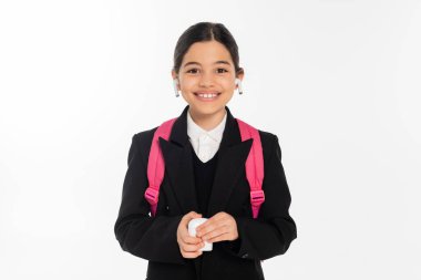 Üniformalı gülümseyen kız çantalı ve kablosuz kulaklık takıyor.