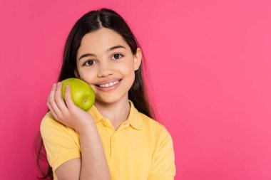 portrait of happy brunette girl holding green and fresh apple isolated on pink, vibrant backdrop clipart