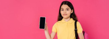 Esmer liseli kız elinde boş ekranlı akıllı telefonu tutuyor ve pembe pankarttaki kameraya bakıyor.