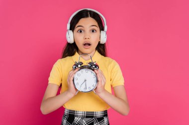 Kablosuz kulaklıklı şok kız elinde klasik çalar saat, pembe, öğrenci hayatında izole edilmiş.