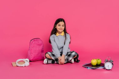 happy schoolgirl sitting near backpack, notebooks, headphones, green apples, vintage alarm clock clipart