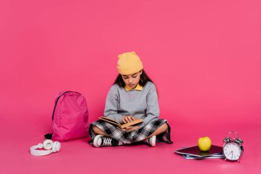 schoolgirl in beanie hat reading book, sitting near headphones, apple, backpack, alarm clock clipart