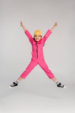 Moda şapkalı ve pembe elbiseli heyecanlı kız ellerini griye uzatmış atlıyor, iyi eğlenceler.