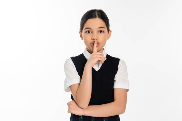 Брюнетка школьница показывает знак молчания и глядя на камеру изолированы на белом, шшшш, палец возле губ