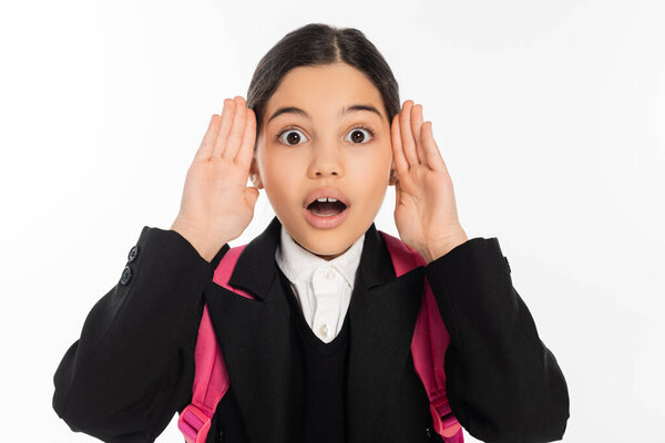 shocked schoolgirl in uniform looking at camera isolated on white, student life, hands near face