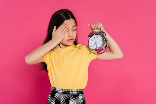 stock image brunette schoolgirl looking at vintage alarm clock isolated on pink, back to school concept,