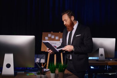 focused bearded businessman working with documents near computer monitor in office, night shift clipart
