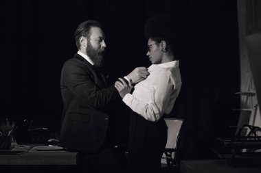 black and white photo of businessman undressing african american woman in night office, side view clipart