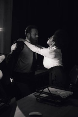 black and white image of businessman undressing near passionate african american woman in office clipart