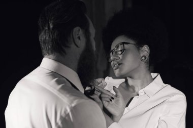 monochrome photo of african american woman in eyeglasses seducing bearded businessman in office clipart