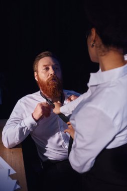 tutkulu bir Afrikalı Amerikalı, gece ofiste sakallı bir iş adamının kravatını çekiyor.