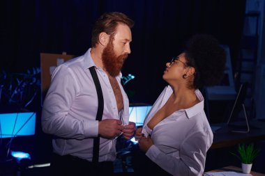 Sakallı iş adamı ve Afrikalı Amerikalı kadın soyunup birbirlerine bakıyorlar.