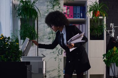 Zarif afro-amerikan iş kadını belgelerle fotokopi makinesini gece ofiste açıyor.