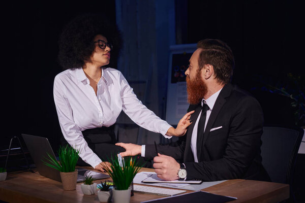 african american businesswoman tempting bearded man at workplace, love affair in night office