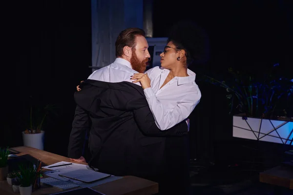 情熱的な異人種間のカップルは 夜のオフィスで職場で抱擁し 仕事のロマンス — ストック写真