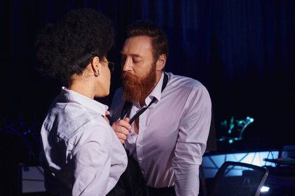 handsome bearded businessman undressing near hot african american woman at night, love in office