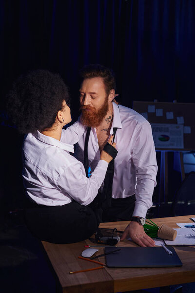 hot african american woman seducing bearded tattooed colleague near mess on work desk in office