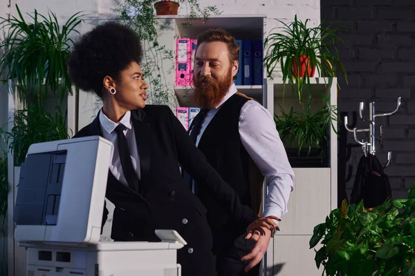 stock image bearded businessman seducing indignant african american woman near copier in office, harassment