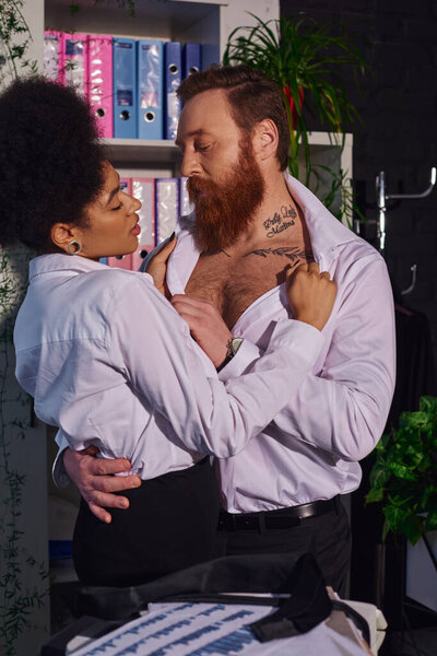 seductive african american woman undressing bearded tattooed businessman, seduction in night office