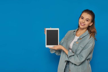 Mavi arka planda boş ekranlı dijital tablet tutan mutlu genç kadın, sosyal medya