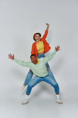 Şaşırmış genç bir kadın, gri arka planda, özgürlük ve eğlence içinde mutlu bir Afrikalı Amerikalı erkeğin yanında yükseğe zıplıyor.