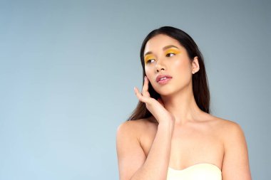 Asyalı kadın, cesur makyajlı, straplez bluzlu, mavi, parlak tenli ve gençken soyutlanmış.
