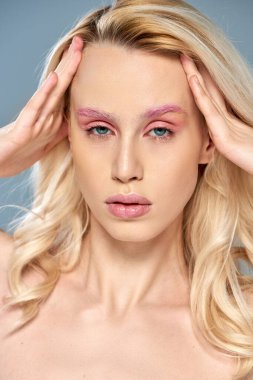 Pembe göz makyajlı, sarı saçlı, gri arka planda poz veren büyüleyici bir model, kadınsı bir güzellik.